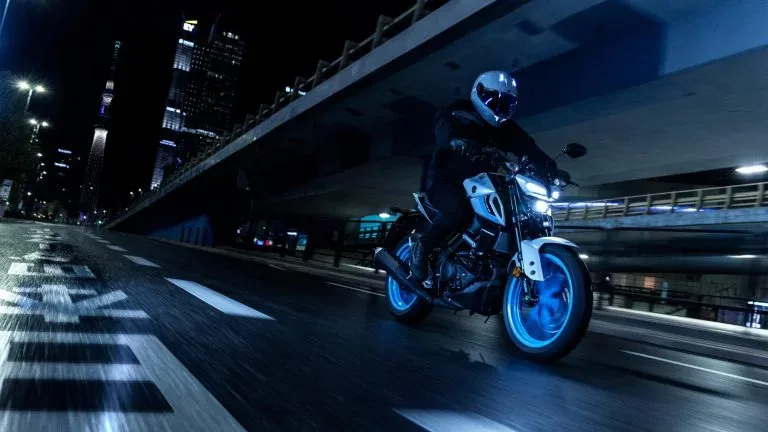 Yamaha-motor met blauwe velgen rijdt 's nachts over een verlichte stadsweg