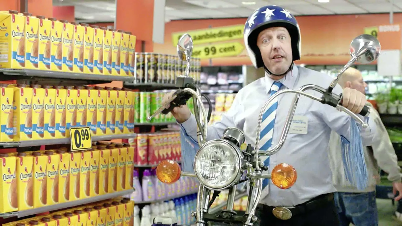 Harry Piekema als supermarktmanager meneer Van Dalen op een motor tussen de schappen in een reclame van Albert Heijn
